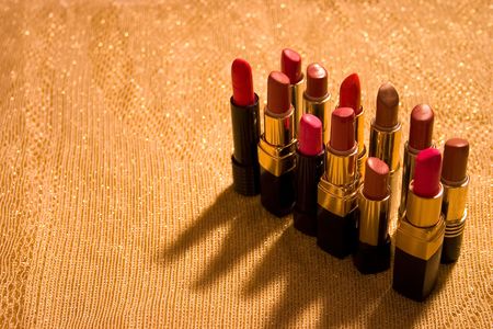 Background of gold shiny material with a dozen open tubes of lipstick.の写真素材