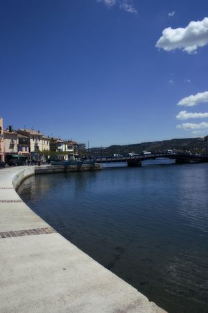 Blue sky and turquoise water, a few puffy white clouds, a curving pier and congested bridge in Martigues, France.の写真素材