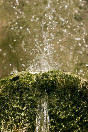 Looking down at water spilling and splashing about in an old sunlit fountain.