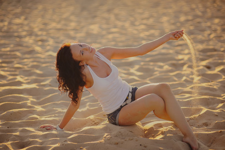Young Woman sitting on the beach playing with sandの写真素材
