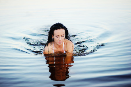 young  brunette woman swimming in lake, sunset lightの写真素材