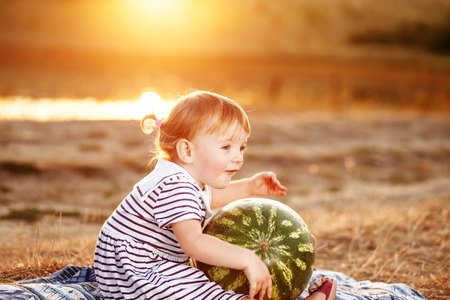 Lovely girl kid sitting wih big watermelon at countryside, having fun.の写真素材