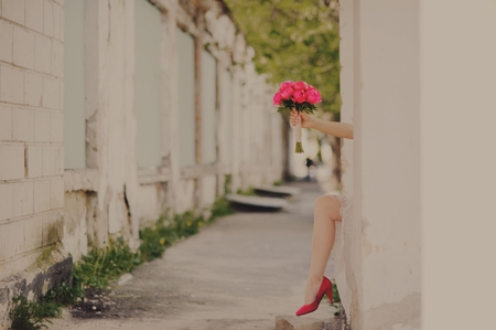 Tricky bride with wedding bouquet at street showing red shoes.の写真素材