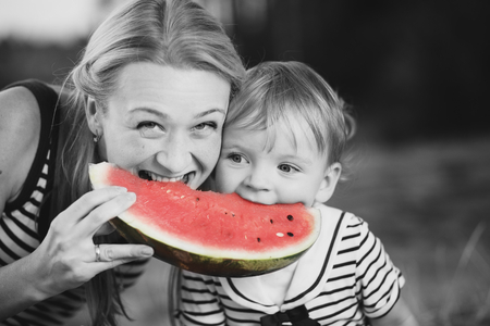 Cute girl kid  wih mom eating big watermelon at countryside, having fun. Black and white with color accent.の写真素材