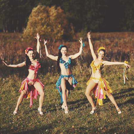 Three funny attractive females wearing dresses, dancing in fieldの写真素材