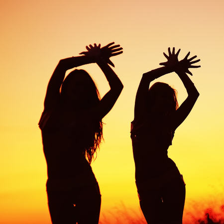 silhouettes of young women against sunset skyの写真素材