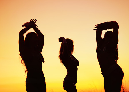 silhouettes of young women against sunset skyの写真素材