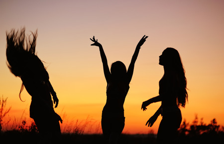 Girls have fun. Silhouettes of young women against sunset skyの写真素材
