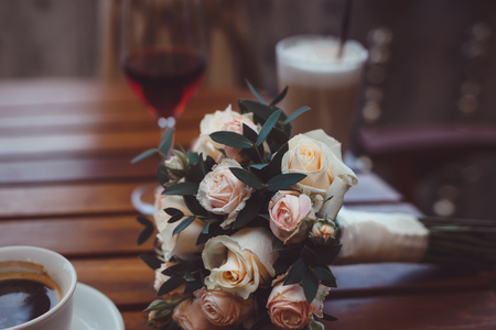 luxury wedding bouquet of tiny roses  laying on wooden table in cafe between coffee cappucino and glass of vine, film like colorsの写真素材