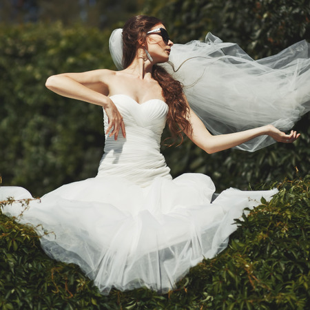Stylish bride with flying veil. Young happy  fiancee in park.の写真素材