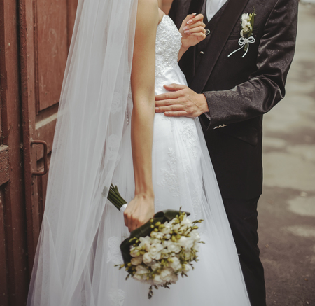Groom and Bride embracing next to red brick wall. Hands of newlyweds  together. Wedding Couple.の写真素材
