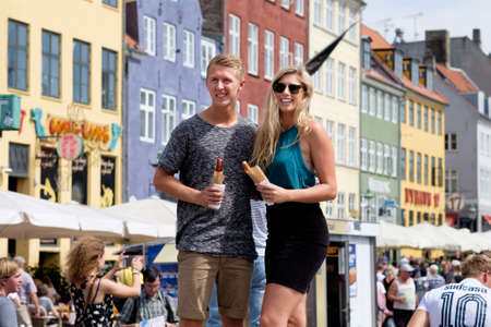 Copenhagen, Denmark 23 July 2016. A couple of tourists with hot dogs in their hands posing for the camera in the most tourist area of Copenhagen Nyhavn.のeditorial素材