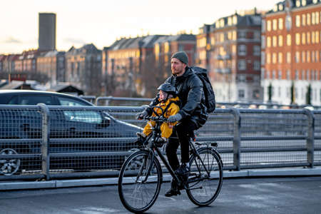 Copenhagen, Denmark 29 November 2019. Young father rides a bicycle with a child dressed in yellow overalls and helmet. People in Copenhagen, lifestyle of Denmark.のeditorial素材