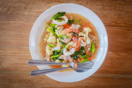 Seafood in thick gravy with thin rice noodles on white plate on wooden table, Food served with top viewの写真素材