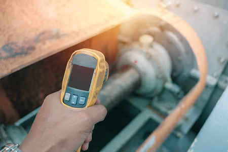 Hand holding of infrared thermometer inspection temperature machinery for preventive maintenance in factoryの写真素材