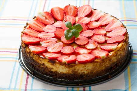 Photo of a whole good looking vanilla cheesecake topped with sliced strawberries and mint.の写真素材