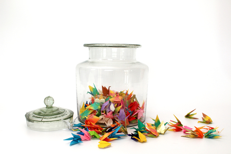 colorful paper origami birds in the cleared glass jar on white backgroundの写真素材