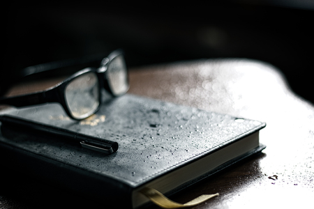 Glasses and pen are placed on the books on the wood table.の写真素材