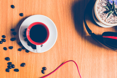 top view of a cup of  hot coffee on the brown table floor with some coffee beans  ,headphone and cactus in flowerpot for backgroundの写真素材