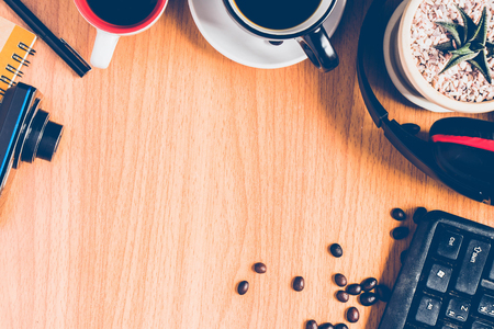 top view of  the wooden brown desk or brown table with many things ,a keyboard, a headphone, a cactus in the white flowerpot, a cup of coffee ,  many coffee beans ,a pen  and a camera for backgroundの写真素材