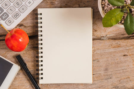 top view of a sketchbook  or a notebook,a datebook with a pen,a mobile phone, a calculator,an apple, and a cactus in the flowerpot on the brown wood floor for backgroundの写真素材