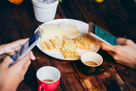 people are playing ,using mobile phone ,drinking coffee,eating biscuit on brown wood table.の写真素材