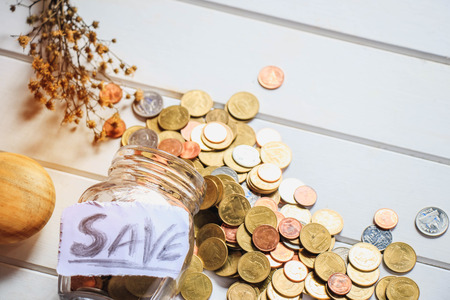 many money coins in the glass bottle with the letter "SAVE"on the top and some dried grass flower next to it for blackground.の写真素材