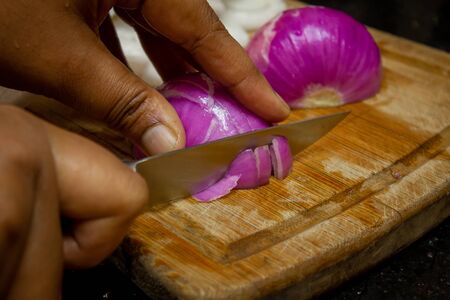 Female cutting red onion with knife over a chopping board