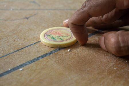 Person ready to strike the coins in carrom board game. Multiplayer board game with good fun time.の写真素材