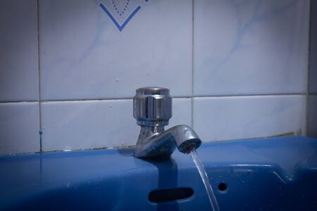 An open tap with water flowing in wash basinの写真素材