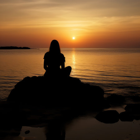 Silhouette of a woman sitting on a rock and looking at the sunsetの素材