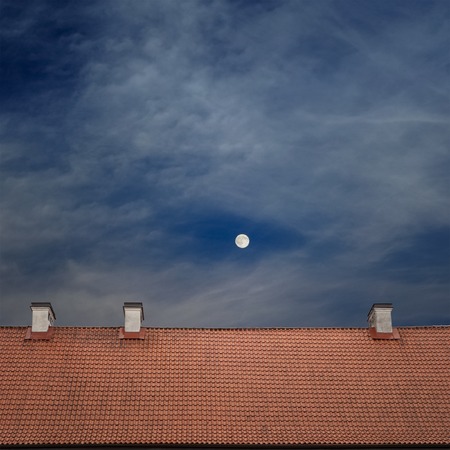 tiled top of the roof, cloudy blue sky and the moon at nightの写真素材