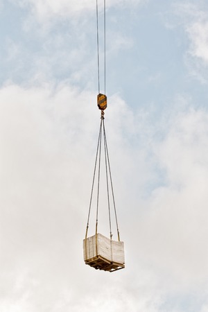 heavy load of bricks hanging on the hook of a crane, blue cloudy sky backgroundの写真素材