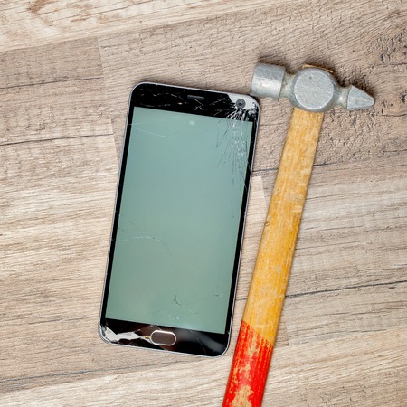 Broken phone screen on a wooden floor with an old hammer