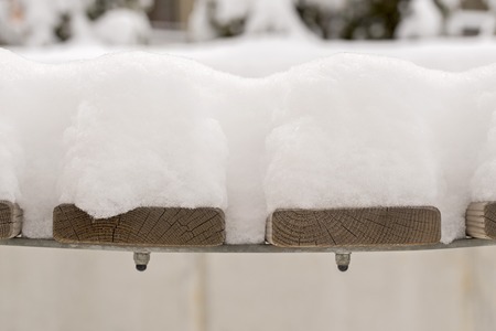 snow on a brown wooden bench in the yardの写真素材