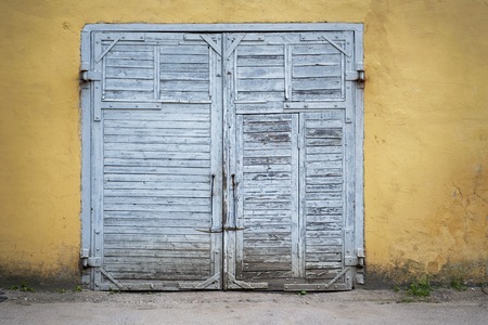Large grey grunge wooden plank door, dirty yellow stucco wall backgroundの写真素材