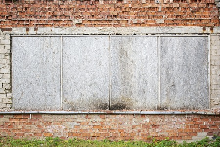 Abandoned grunge cracked brick wall with boarded up windows.
