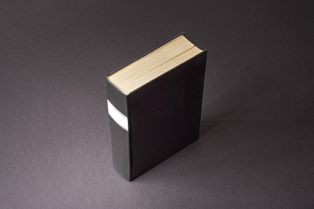 Black book with white frame on spine standing a dark paper surface.の写真素材