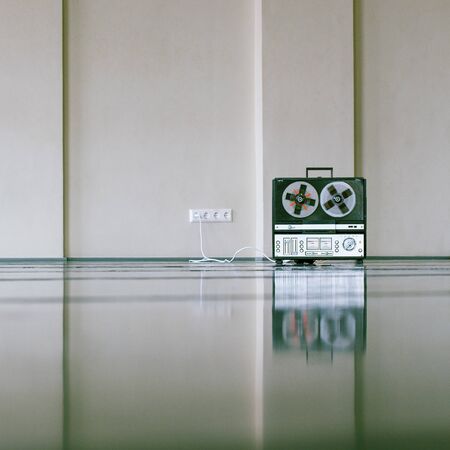 vintage analog magnet tape recorder standing on the floor near wall.