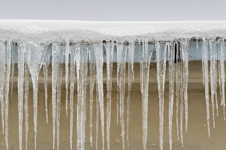 Big icicles hang from the roof of a houseの写真素材