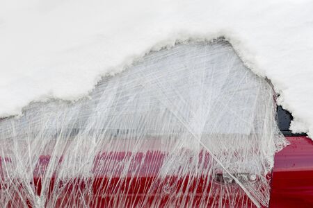 Front window of abandoned car wrapped in plastic and covered with snowの写真素材