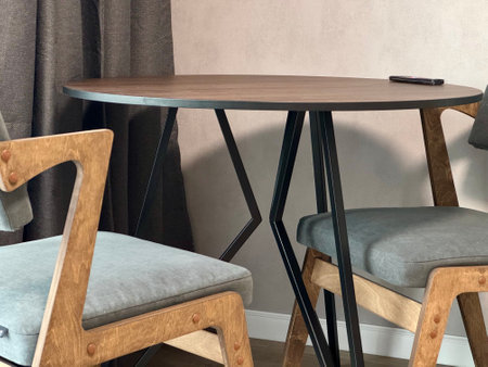 Modern round wooden table with grey cushioned chairs in a minimalist dining area perfect for small apartments. Cozy indoor setting for contemporary home decor.の写真素材