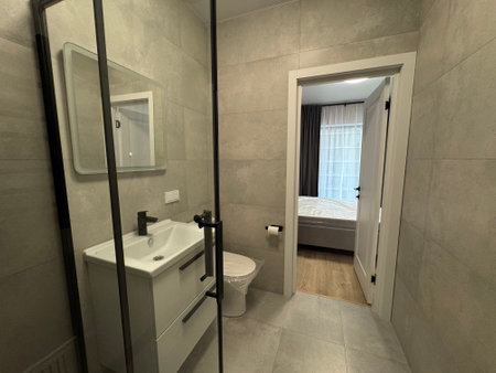 Freshly renovated modern bathroom with a glass shower, illuminated mirror, white sink, and sleek toilet.の写真素材