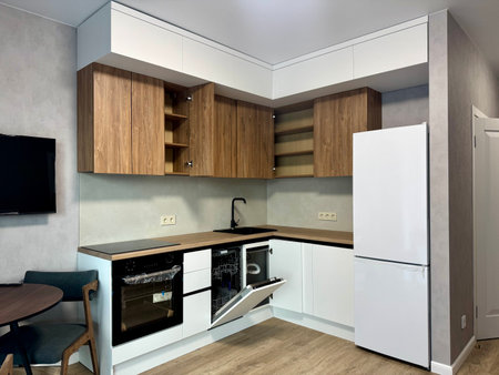Freshly renovated modern kitchen with white cabinets, wooden countertop, and built-in oven. Features a sleek sink, refrigerator, and minimalist design.の写真素材