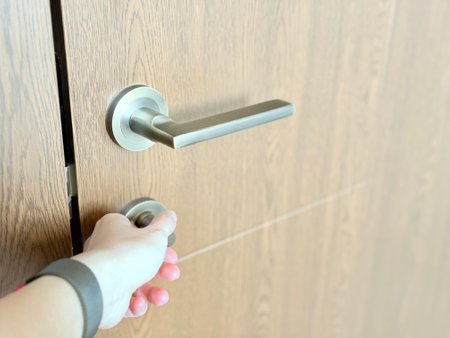 A close-up of a hand turning a modern metal thumb-turn lock on a wooden door with a sleek handle.の写真素材