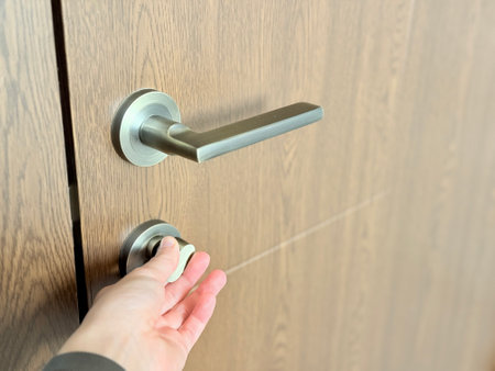 A close-up of a hand turning a modern metal thumb-turn lock on a wooden door with a sleek handle.の写真素材
