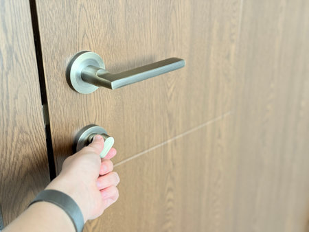 A close-up of a hand turning a modern metal thumb-turn lock on a wooden door with a sleek handle.の写真素材