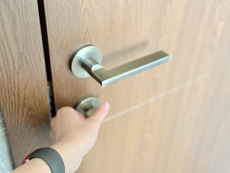 A close-up of a hand turning a modern metal thumb-turn lock on a wooden door with a sleek handle.の写真素材