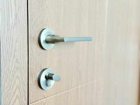 A close-up of a wooden door with a modern metal handle and thumb-turn lock.の写真素材