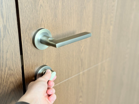 A close-up of a hand turning a modern metal thumb-turn lock on a wooden door with a sleek handle.の写真素材
